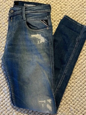 Replay Anbass blå jeans, W30 L32 - Säljer ett par Replay Anbass jeans i klassisk blå färg med slitningar framtill. Jeansen har Replay-logga på bakfickan samt läderpatch i midjan. Tillverkade i mjukt bomullsmaterial med lite stretch.