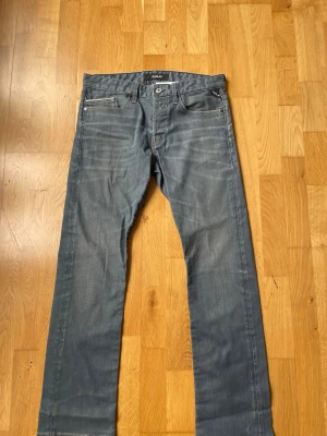 Blå raka jeans från Replay - Snygga blå jeans från Replay med raka ben och klassisk femficksmodell. Jeansen har knäppning med knappar och diskreta slitningar framtill för en cool look. Perfekta för dig som gillar en avslappnad men stilren stil.