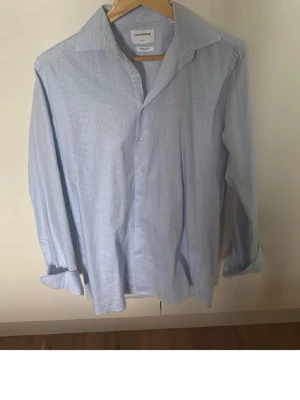 Randig skjorta från Lindbergh White - Snygg ljusblå och vit randig skjorta från Lindbergh White. Slim fit-modell i mjuk, ekologisk bomull med superflex för extra komfort. Klassisk krage, långa ärmar och knappar framtill. Perfekt för en clean och stilren look.