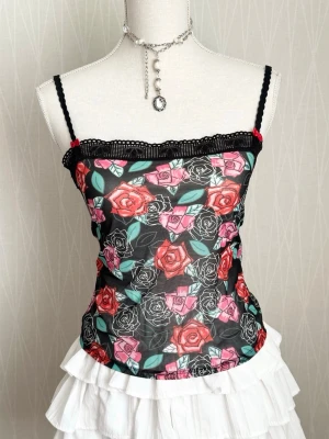 Blommig mesh linnetopp med spets - Snygg linnetopp i mesh med blommigt mönster i rosa och rött på svart botten. Toppen har tunna svarta axelband, spetskant upptill och figurnära passform. Perfekt för dig som gillar en romantisk och edgy stil.