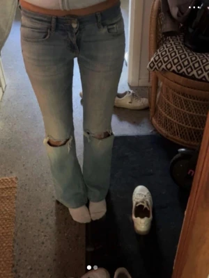 Ljusblå slitna jeans med hål - Säljer ett par ljusblå jeans med raka ben och slitna hål vid knäna. Jeansen har klassisk femficksmodell och normal midja. Perfekta för en avslappnad och trendig look.