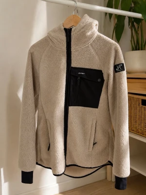 Beige teddyjacka  - Mysig beige teddyjacka från RVRC med svart bröstficka, dragkedja framtill och huva. Jackan har svarta detaljer vid ärmslut och nederkant samt logga på ärmen och ryggen. Perfekt för kyliga dagar och har en avslappnad passform.
