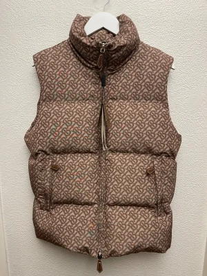 Beige dunväst från Burberry med monogram - Snygg beige dunväst från Burberry med ikoniskt all-over monogrammönster i brunt. Västen har hög krage, dragkedja framtill med läderdetalj och två fickor. Insidan är slät och brun. Perfekt för lager-på-lager och streetstyle.