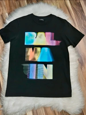 Svart Balmain t-shirt med färgglatt tryck - Cool svart t-shirt från Balmain med ett stort, färgglatt grafiskt tryck framtill. T-shirten har klassisk passform och är gjord i mjuk bomull, perfekt för en trendig och avslappnad stil.
