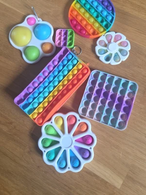Samling pop it och fidget toys - Säljer ett gäng pop it och fidget toys i olika former och färger. Här finns bland annat regnbågsfärgade pop it i rund och fyrkantig form, blomformade fidget toys och en pop it-necessär. Perfekt för dig som gillar att pilla och stressa ner.
