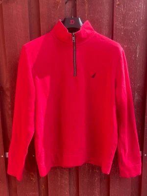 Röd halfzip tröja från Nautica - Riktigt snygg röd långärmad tröja från Nautica med halfzip och hög krage. Tröjan har en liten broderad logga på bröstet och är gjord i mjukt bomullsmaterial. Passar bra på någon 175-180cm