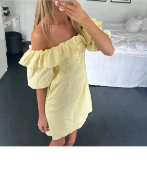 Gul offshoulder kortklänning - Söt gul kortklänning med offshoulder och volangdetalj upptill. Klänningen har puffiga korta ärmar och en avslappnad passform, perfekt för varma dagar. Tillverkad i ett lätt tyg som känns skönt mot huden.