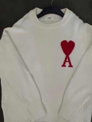 Ami Paris Heart Logo Stickad Tröja Vit  - Helt ny Ami Paris stickad tröja i vitt. Aldrig använd och i mycket fint skick.  Säljs då den inte används. Stilren och tidlös modell med den välkända Ami de Coeur-loggan på bröstet.  Hör gärna av dig om du vill ha fler bilder eller information.