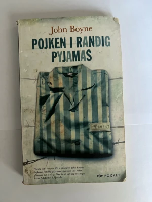 Pojken i randig pyjamas pocketbok - En gripande roman av John Boyne om vänskap och grymhet under andra världskriget. Pocketutgåva med omslag i vitt och blågrönt, prydd med en randig pyjamas och taggtråd. Perfekt för dig som gillar starka berättelser och historiska teman.