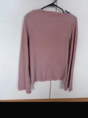 Rosa långärmad tröja - En enkel och stilren rosa långärmad tröja med diskret strukturmönster. Tröjan har rak passform och mjukt material som känns skönt mot huden. Perfekt att matcha med jeans eller kjol för en avslappnad look.