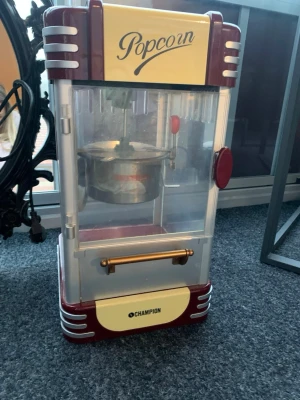 Retro popcornmaskin från Champion - Säljer en retroinspirerad popcornmaskin från Champion i röd och gul plast och metall. Maskinen har genomskinliga sidor, en inbyggd gryta och två knappar på ovansidan för värme och belysning. Perfekt för hemmabio eller filmkvällar.