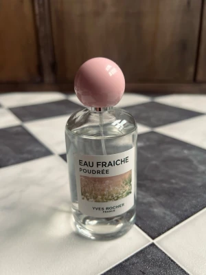 Eau Fraîche Poudrée parfym Yves Rocher 100ml - Eau Fraîche Poudrée från Yves Rocher är en parfym i en genomskinlig glasflaska med rund, ljusrosa kork. Flaskan har en enkel och stilren etikett med blommotiv och svart text. Doften är inspirerad av pudriga och fräscha toner.