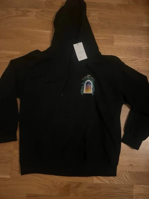 Svart hoodie från Casablanca - Svart hoodie från Casablanca med tryck på bröstet och klassisk känguruficka. Märket syns tydligt på bröstet tillsammans med ett färgglatt motiv. Hoodien har dragsko i huvan och är tillverkad i mjukt material för en skön känsla.