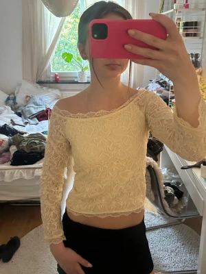Gul spets offshoulder topp - Söt gul offshoulder topp i spets med lång ärm och fina spetsdetaljer längs kanterna. Croppad modell som ger en trendig vibe och passar perfekt till både kjol och jeans. Blommigt mönster i spetsen för extra detalj.
