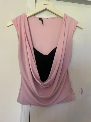 Rosa draperad topp❤️ - Snygg ljusrosa topp från Acne med draperad front och svart detalj under urringningen. Ärmlös modell med mjukt, stretchigt material som ger en smickrande passform. Perfekt för dig som vill ha en unik och trendig look. Vintage❤️