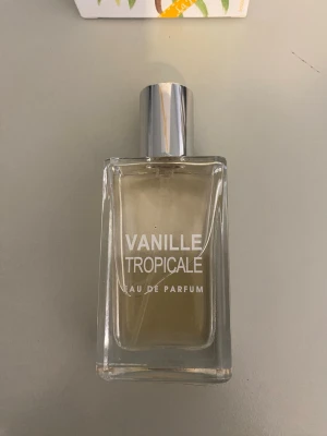 Vanille Tropicale Eau de Parfum - Vanille Tropicale Eau de Parfum från Jeanne Arthes kommer i en stilren, rektangulär glasflaska med silverfärgad kork. Doften har en tropisk och söt vaniljkaraktär. Flaskan är transparent och etiketten har vit text. Förpackningen har blommigt motiv. Helt ny testad en gång. 