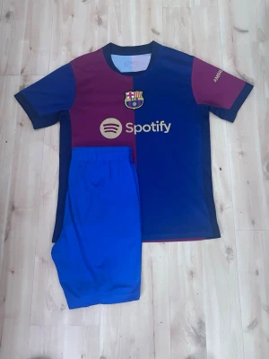 FC Barcelona matchställ Spotify - Säljer ett FC Barcelona matchställ med tröja och shorts. Tröjan är blå och vinröd med klubbmärke och Spotify-logga på bröstet samt Nike-logga. Korta ärmar och rund hals. Shortsen är helblå och har resår i midjan. Perfekt för fotbollsträning eller match.