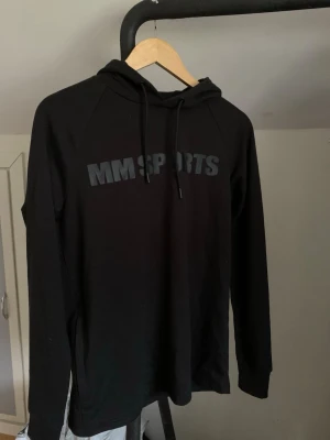 Svart hoodie från MM Sports - Snygg svart hoodie från MM Sports med tryckt logga på bröstet. Klassisk modell med huva och dragsnören, samt långa ärmar. Perfekt för gymmet eller chill. Tillverkad i mjukt material som känns skönt mot huden. Hör av dig vid minsta fundering och pris kan diskuteras! 🤩💯