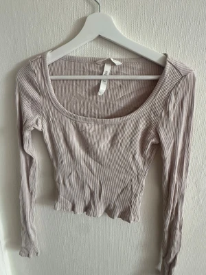 Ljusbeige ribbad croppad topp H&M - Trendig ljusbeige croppad topp från H&M med ribbad struktur. Toppen har lång ärm och en bred, rundad urringning som ger en snygg siluett. Perfekt att matcha med höga jeans eller kjol för en cool vardagslook.