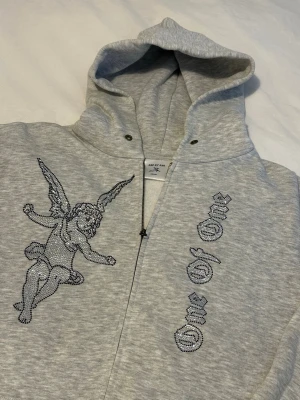 Grå One of One rhinestone hoodie  - Säljer en grå zip hoodie från One of One. Hoodien har huva och dragkedja framtill. Tillverkad i mjukt sweatshirtmaterial, perfekt för en chill och unik stil.