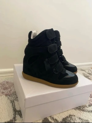 Svarta Isabel Marant sneakers  - Snygga svarta high top sneakers med flera kardborreband och brun sula. Skorna har en chunky siluett och är tillverkade i mockaliknande material med detaljer i textil. Perfekta för dig som vill ha en statement-look till vardagsoutfiten.