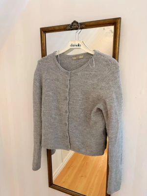 Ljusgrå kofta  - Mysig ljusgrå kofta  med rund halsringning och knappar framtill. Koftan har lång ärm och är stickad i ett mjukt material som känns skönt mot huden. Enkel och stilren design som passar till många olika looks.