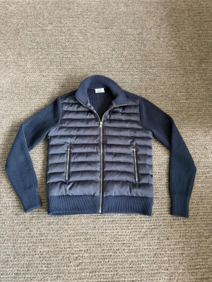 Cardigan - Snygg mörkblå pufferjacka från L.B.M. med quiltad front och stickade ärmar samt krage. Jackan har två dragkedjeförsedda fickor framtill och ribbade muddar vid ärmslut och nederkant. Perfekt för kalla vinterdagar och ger en modern, sportig look.