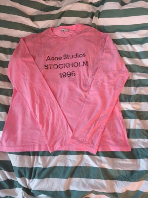 Rosa långärmad t-shirt Acne Studios - Snygg rosa långärmad t-shirt från Acne Studios med tryck 'Acne Studios STOCKHOLM 1996' på bröstet. Klassisk rund halsringning och avslappnad passform. Perfekt för dig som gillar streetwear och vill ha något från ett ikoniskt svenskt märke.