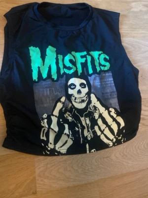 Svart Misfits ärmlös linnetopp - Cool svart ärmlös linnetopp med stort grönt Misfits-tryck och skelettgrafik på framsidan. Perfekt för dig som gillar bandmerch och vill sticka ut med en edgy stil.