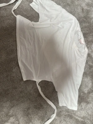 Vit knyt topp från Nelly - Säljer en vit knyt i ryggen topp från Nelly  med knytband i sidan. Toppen har korta ärmar och rund halsringning med ribbad kant. Perfekt för dig som gillar en enkel men trendig look. Jag skulle säga att den är lite liten i storlek så skulle snarare säga S