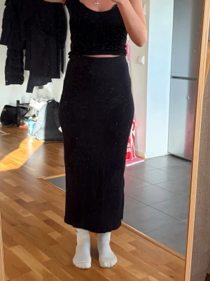 Svart ribbad långkjol med slits - Snygg svart ribbad långkjol med slits på sidan. Kjolen har en tight passform och hög midja. 