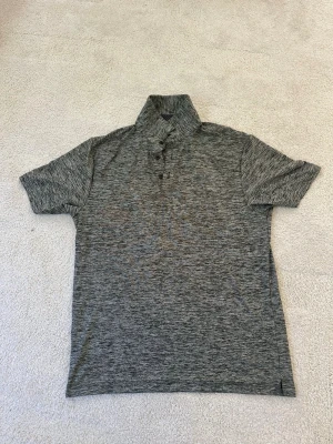 Gråmelerad polotopp - Snygg gråmelerad polotopp med korta ärmar och knappslå framtill. Tillverkad i mjukt och lätt material som passar perfekt till många olika stilar. Enkel och stilren design utan synliga loggor eller tryck.