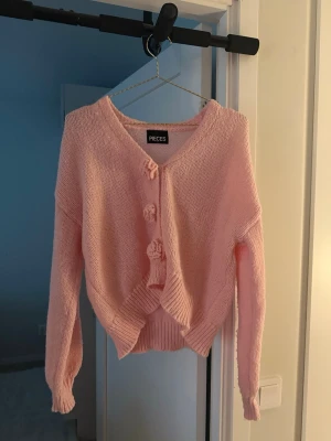 Rosa kofta från Pieces med rosetter - Söt ljusrosa stickad kofta från Pieces med v-ringning och rosettknappar framtill
