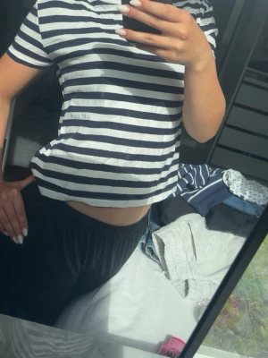 Randig kortärmad t-shirt i bomull - Säljer en klassisk kortärmad t-shirt med marinblå och vita horisontella ränder. T-shirten har en avslappnad passform och är gjord i mjuk bomull, perfekt för en enkel och stilren look.