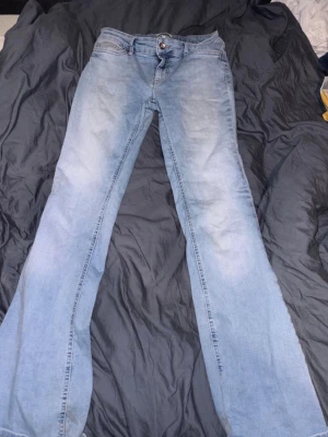 Ljusblå lågmidjage bootcut jeans - Säljer ett par ljusblå bootcut jeans med klassisk femficksdesign och dragkedja med knapp. Jeansen har en snygg tvättad look och raka ben som går ut något nedtill. Perfekta för en avslappnad och trendig stil.