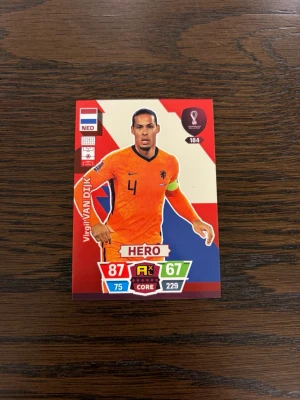 Virgil Van Djik fotbollskort VM 2022 - Samlarfotbollskort från FIFA World Cup Qatar 2022 med spelare från Nederländerna. Kortet har färgerna orange, röd, blå och vit, och visar statistik och specialkategorin HERO. Perfekt för samlare eller spelentusiaster.