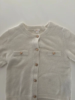 Beige/ vit kortärmad kofta med guldiga knappar - Stickad kortärmad från Gina Young med metalknappar i guld