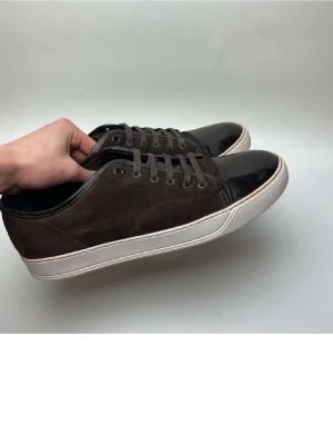 Bruna lanvin - Snygga bruna sneakers från lanvin. Ovandel i mocka och tåparti i blankt läder. Skorna har vita sulor och matchande bruna skosnören. Perfekta för dig som gillar en stilren och klassisk look med en twist. Passar till jeans eller chinos för en avslappnad vibe.