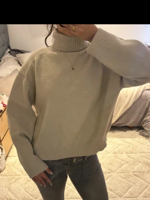 Beige polotröja i oversize - Mysig beige stickad polotröja i oversize-modell med breda ribbade muddar vid ärmslut och nederkant. Lite tajt krage!