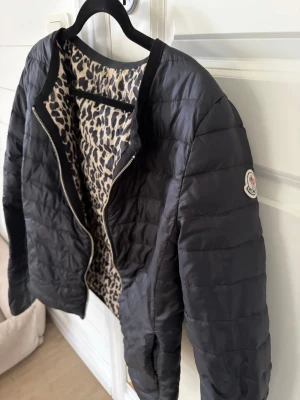 Gammal unik moncler jacka!! - Snygg svart dunjacka från Moncler med quiltad design och dragkedja framtill. Insidan har ett coolt leopardmönster som ger extra edge. Jackan har rundad krage och klassisk Moncler-logga på ärmen. Perfekt för kalla vinterdagar och riktigt trendig look. Jackan är ca 10 år gammal skulle jag tro, bra skick men har sytts in så den är i storlek S, unik, fin, bra skick, bra pris, har ej möjlighet till bild på.