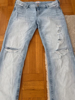 Ljusblå loose ripped jeans  - Säljer ett par ljusblå jeans från gina med slitna detaljer och hål på benen. Jeansen har raka ben och klassisk femficksmodell med den ikoniska vita sömmen på bakfickan. Perfekta för en avslappnad streetstil. På ena balfickan finns ett igensytt litet hål,dom är också uppsydda vid benen men går lätt stt sprätta upp💕