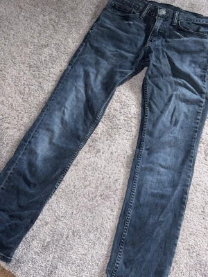 Blå Levi's jeans med raka ben - Säljer ett par klassiska blå Levi's jeans med raka ben och fem fickor. Jeansen har en snygg tvättad look och är tillverkade i slitstark denim. Perfekta för dig som gillar tidlös stil och vill ha ett par jeans som funkar till allt.