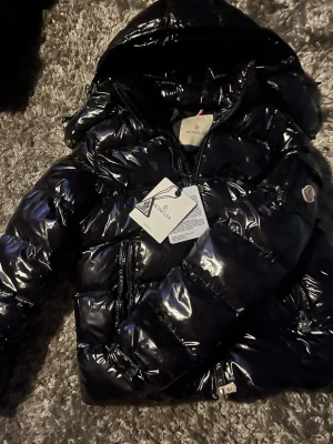 Svart glansig dunjacka från Moncler - Moncler jacka maya köpt 2024 loggans scan funkar samt qr koden passar 150-160 passar både tjej och kille kommer samt med alla tags