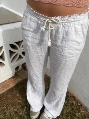 Vita linnebyxor med dragsko - Säljer ett par vita linnebyxor med avslappnad passform och dragsko i midjan. Byxorna har raka ben, sidofickor och är tillverkade i ett luftigt linnematerial som passar perfekt till sommaren. Superenkla att styla med crop top eller skjorta.