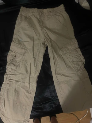 Beige cargobyxor med fickor - Säljer ett par beige cargobyxor med flera stora fickor på sidorna och avslappnad passform. Byxorna har resår i midjan och är tillverkade i ett lätt bomullstyg. Perfekta för en chill och avslappnad stil.