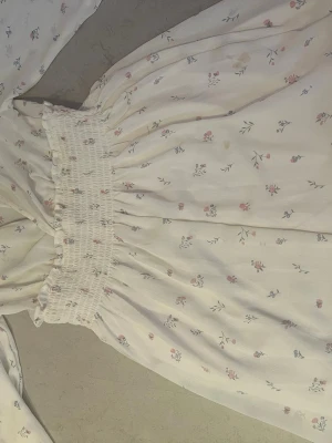 Vit blommig omlottklänning XS - Söt vit kortklänning från lager 157 med små blommor i rosa och blått. Klänningen har omlottliv, smock i midjan och volangdetaljer upptill. Perfekt för sommarens varma dagar och har en luftig känsla. Han en liten fläck men syns knappt men finns en bild den sista bilden visar fläcken 