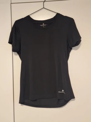 Svart tränings-tshirt från Ronhill  - Svart tränings-tshirt från Ronhill med rund hals och korta ärmar. Tillverkad i ett lätt och snabbtorkande syntetmaterial som passar perfekt för träning. Diskret logga framtill vid nederkanten. Enkel och stilren design.
