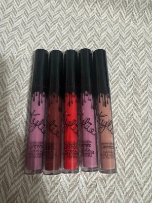 Kylie flytande läppstift set - Säljer ett set med fem matta flytande läppstift från Kylie. Färgerna är lila, mörkröd, klarröd, rosa och nude. Läppstiften kommer i genomskinliga tuber med svart lock och den ikoniska droppdesignen. Perfekt för dig som vill ha flera olika färger att välja mellan.