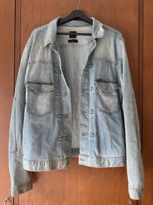 Ljusblå klassisk jeansjacka - Snygg ljusblå jeansjacka med två bröstfickor med lock och knapp, samt knappstängning framtill. Jackan har en avslappnad passform och klassisk krage. Perfekt för dig som gillar en tidlös och cool stil.