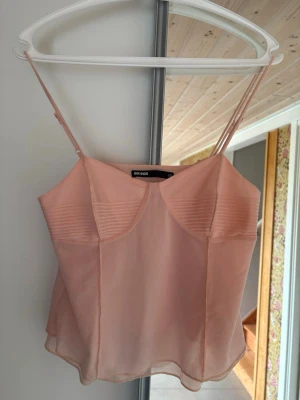 Ljusrosa linnetopp från Bik Bok - Säljer en söt ljusrosa linnetopp från Bik Bok med tunna axelband och lätt transparent material. Toppen har fina sömdetaljer över bysten och en luftig, flowy passform. Perfekt för varma dagar eller lager på lager.
